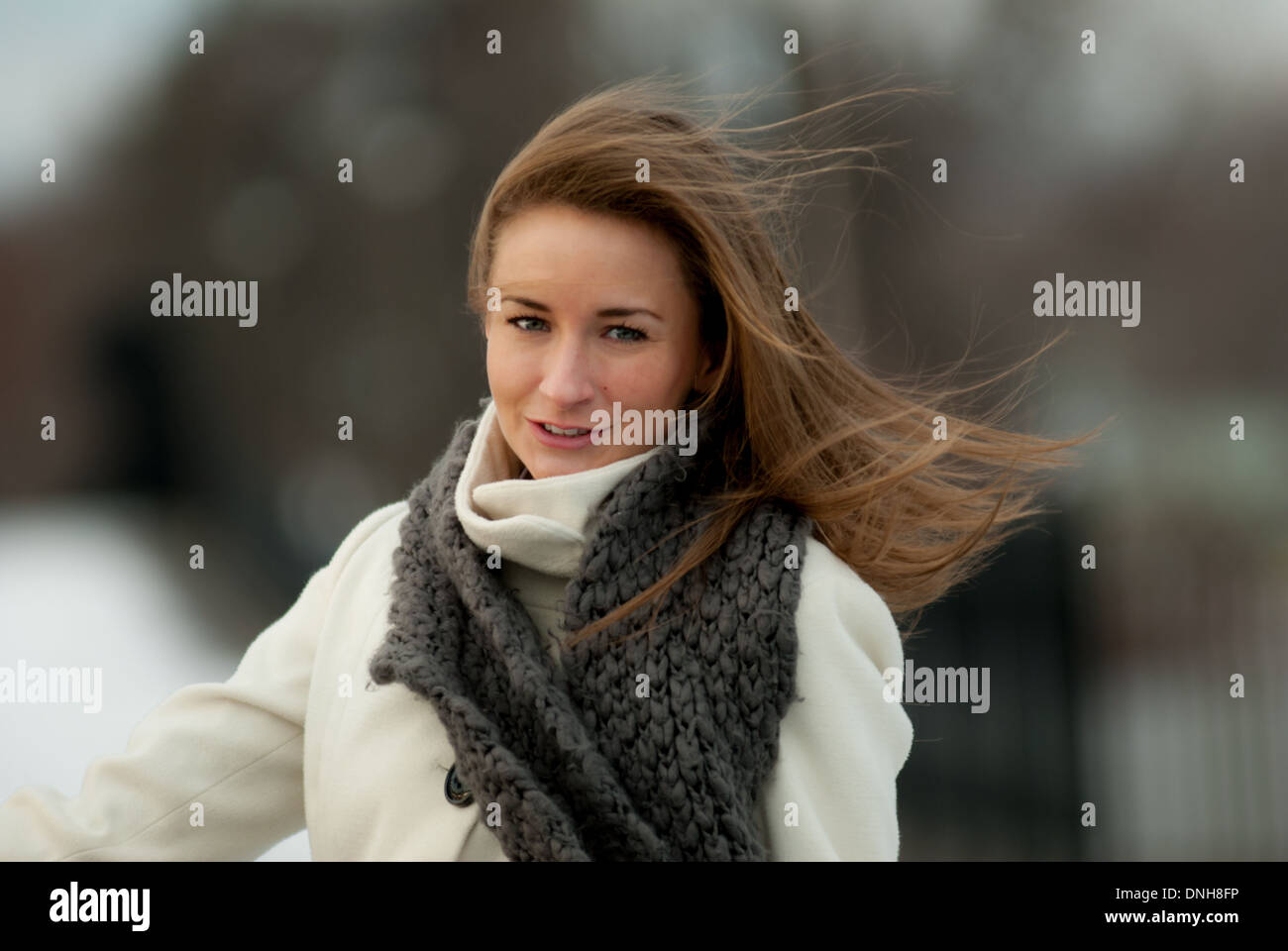 Una giovane e bella donna in un manto bianco e grigio sciarpa sorrisi su un ventoso giorno d'inverno. Foto Stock
