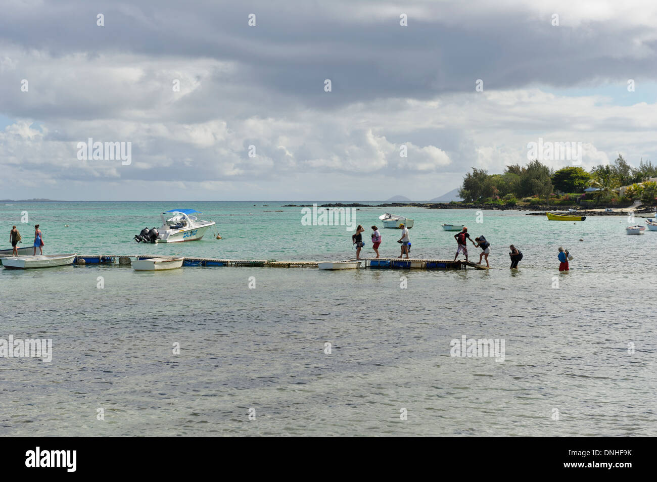 I turisti a piedi nel mare poco profondo a riva per arrivare su una barca veloce, Mauritius. Foto Stock