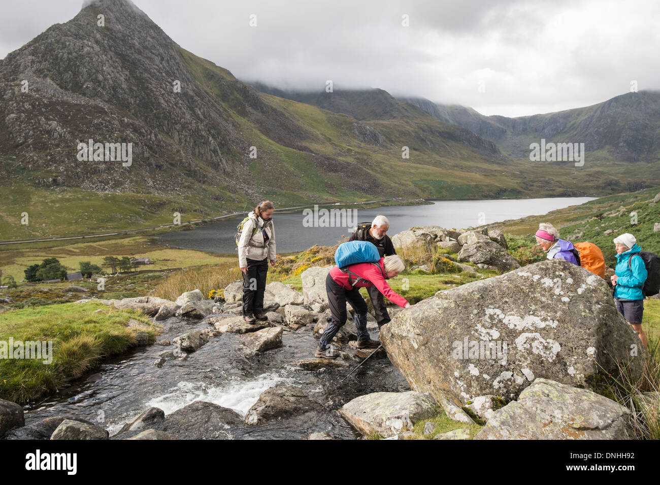 Il camminatore nervoso essendo aiutato attraverso un ruscello di montagna intensificazione su pietre in montagne di Snowdonia. Ogwen Valley North Wales UK Foto Stock