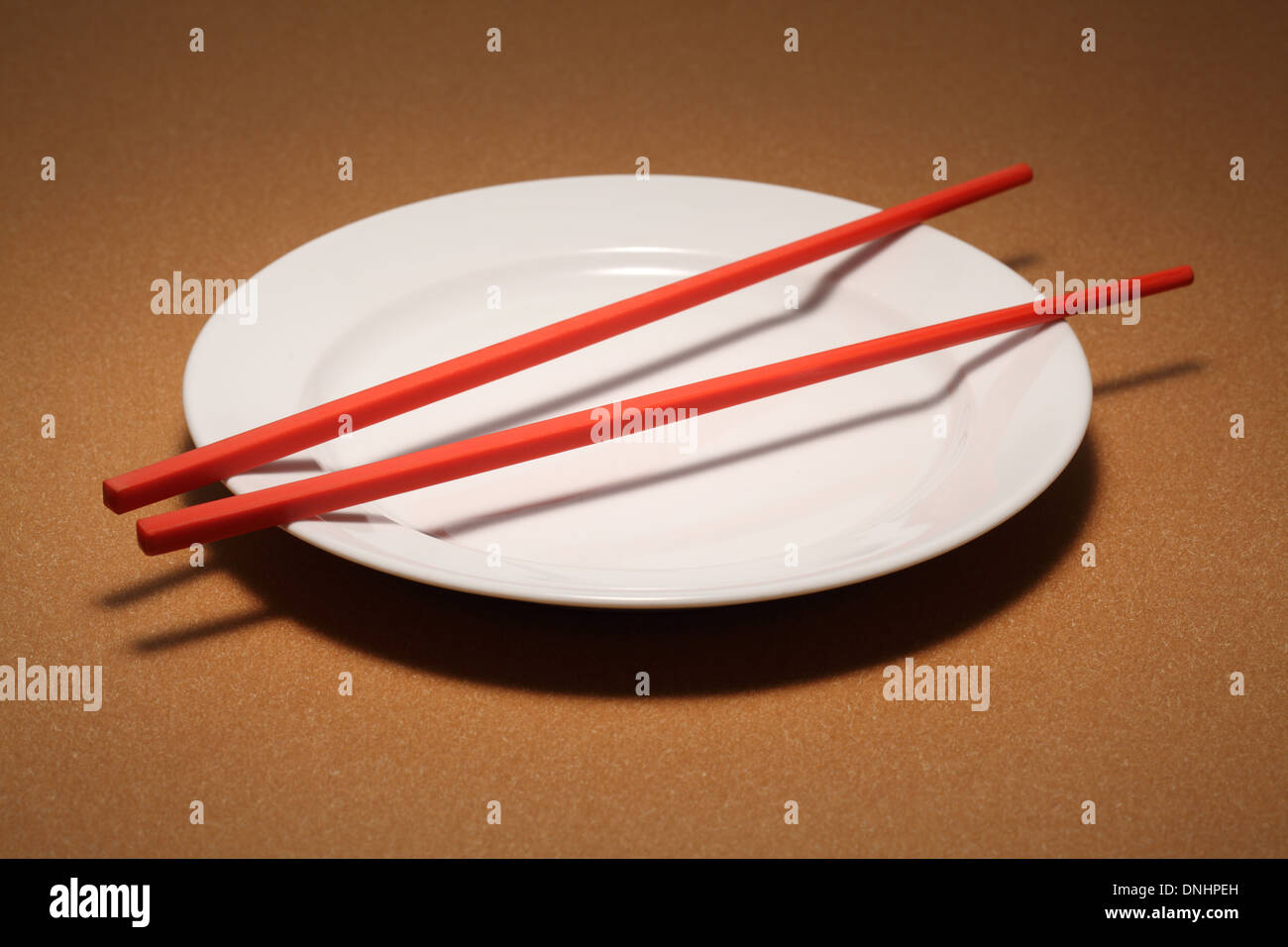 Una coppia di bacchette rosso su bianco vuoto piastra da pranzo. Foto Stock