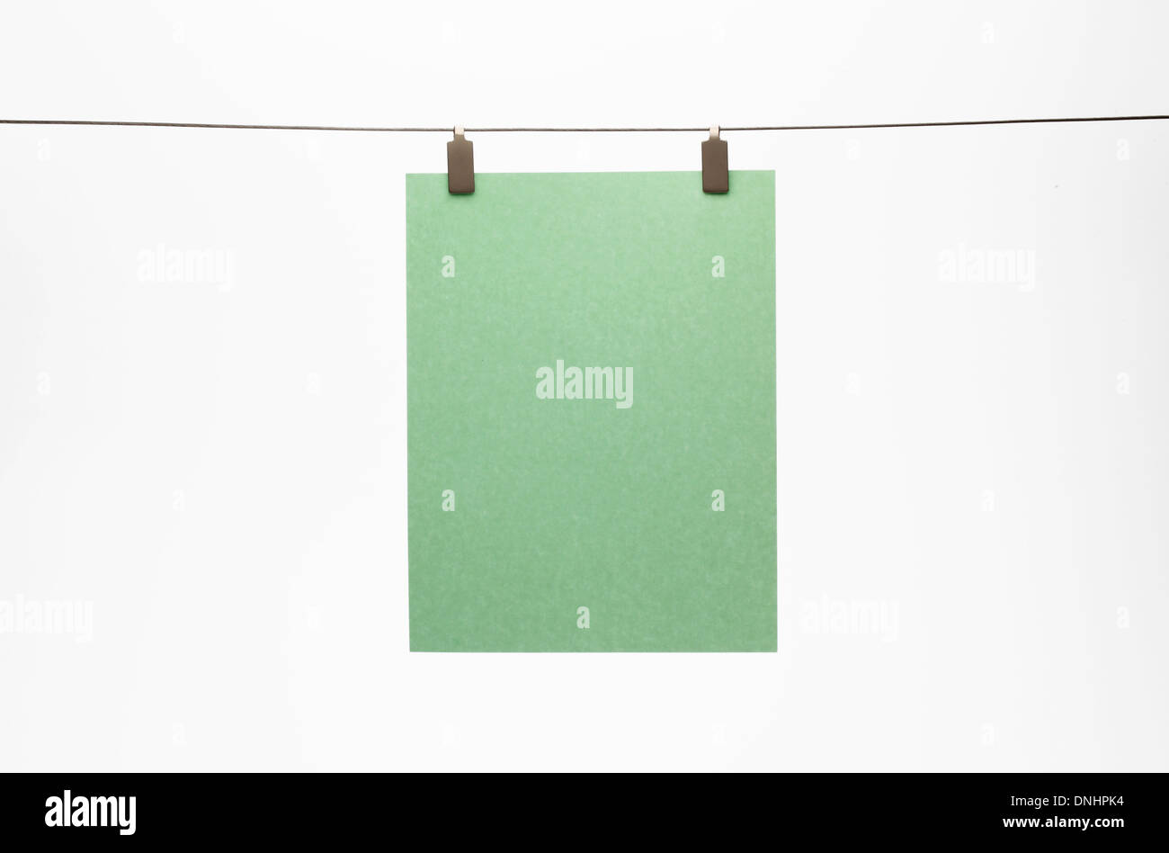 Un pezzo di carta verde appeso con una clip a un filo dritto. Sfondo bianco Foto Stock