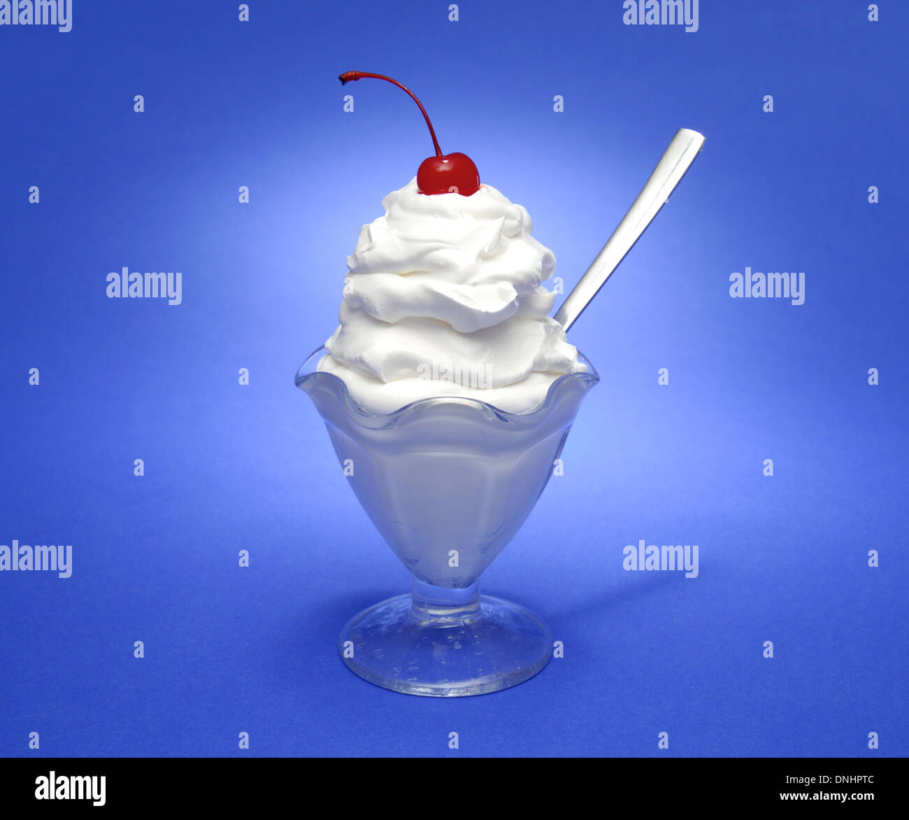 Un bianco crema dessert gelato di vetro con un cucchiaio e una ciliegia di colore rosso sulla parte superiore della panna montata. Foto Stock