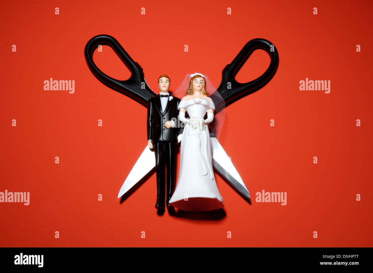 Plastica nozze in miniatura figure con le forbici su uno sfondo di colore rosso. Foto Stock