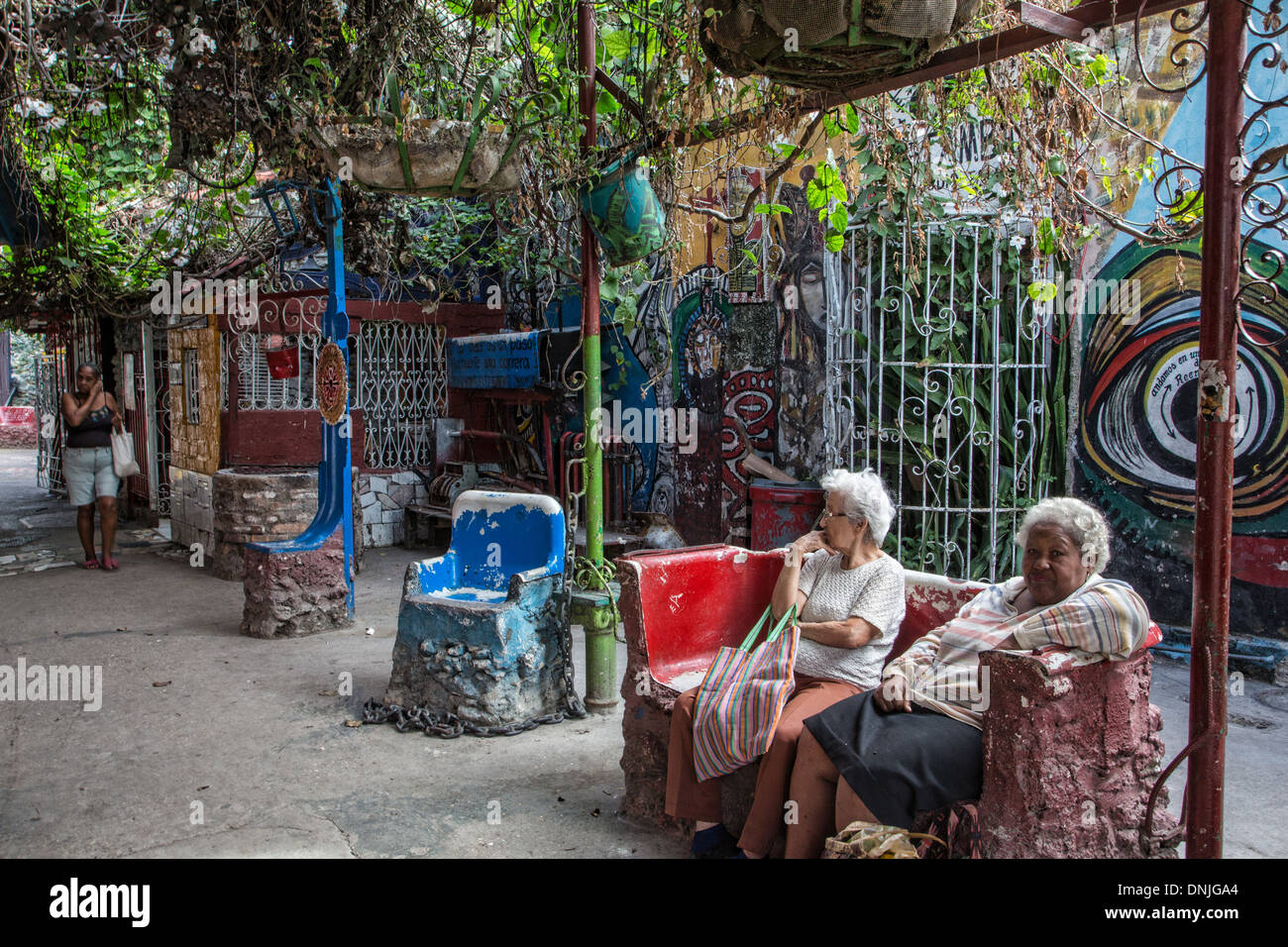 Il vecchio donna seduta davanti al LA SANTERIA dipinti (cubano sincretismo, afro-CARABEAN cultura), opere pittoriche di SALVADOR GONZALEZ ESCALONA dipinta sulla cinta muraria, CALLEJON DE HAMEL, Havana, Cuba, CARAIBI Foto Stock