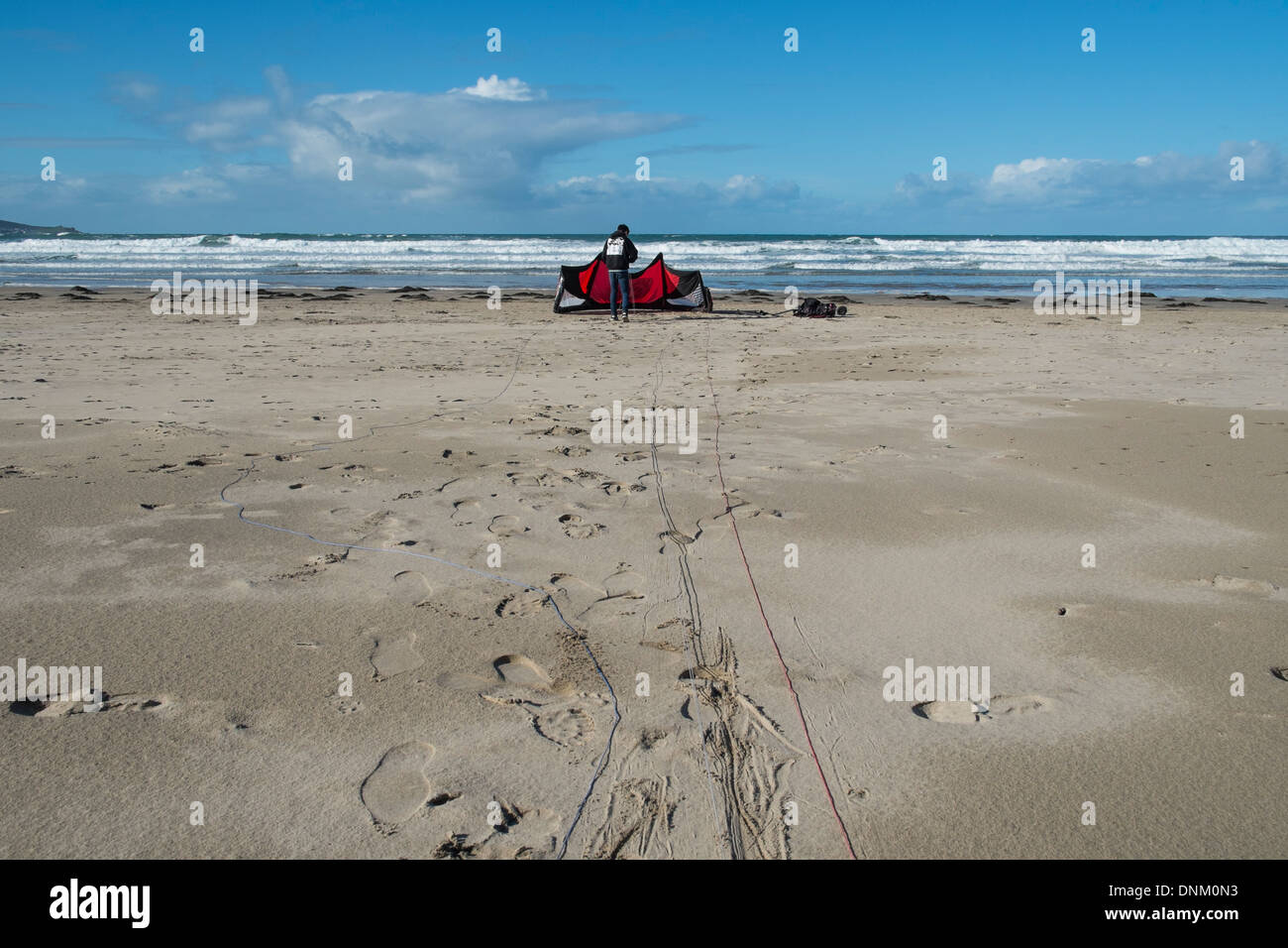 Un giovane uomo imposta un grande aquilone per terra imbarco sulla spiaggia Gwithian, Hayle. Foto di Julie Edwards Foto Stock