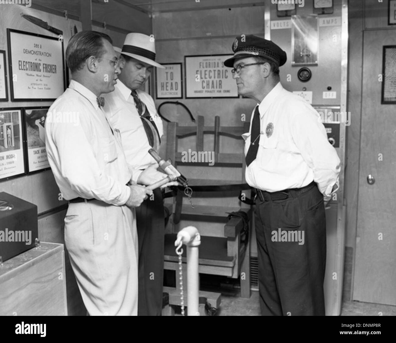 Un'immagine degli anni '1950 che mostra uomini non identificati che parlano accanto a una sedia elettrica a Tallahassee, in Florida. La foto riflette l'impegno del pubblico con questioni di pena capitale durante quell'epoca. Foto Stock