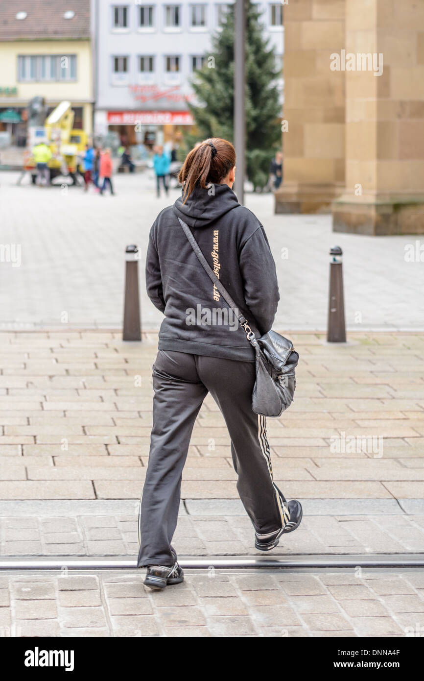 Giovane donna caucasica con capelli castani fatto in una coda di cavallo  vestita di nero Adidas tuta sportiva attraversa una strada con rotaie  incorporati Foto stock - Alamy