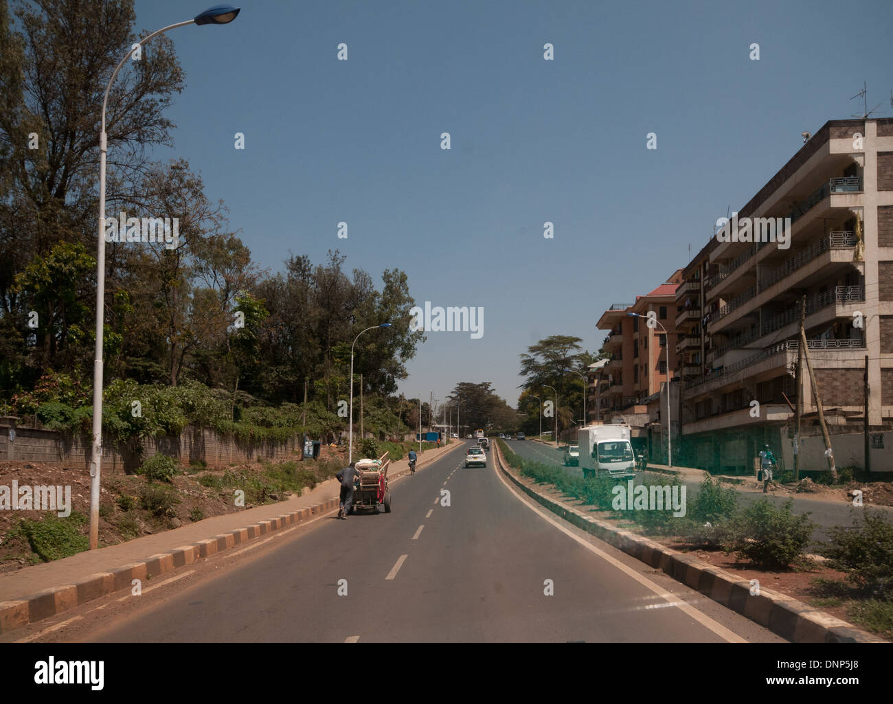 L'uomo spingendo il carrello e il traffico su strada forestale Nairobi Kenya Foto Stock