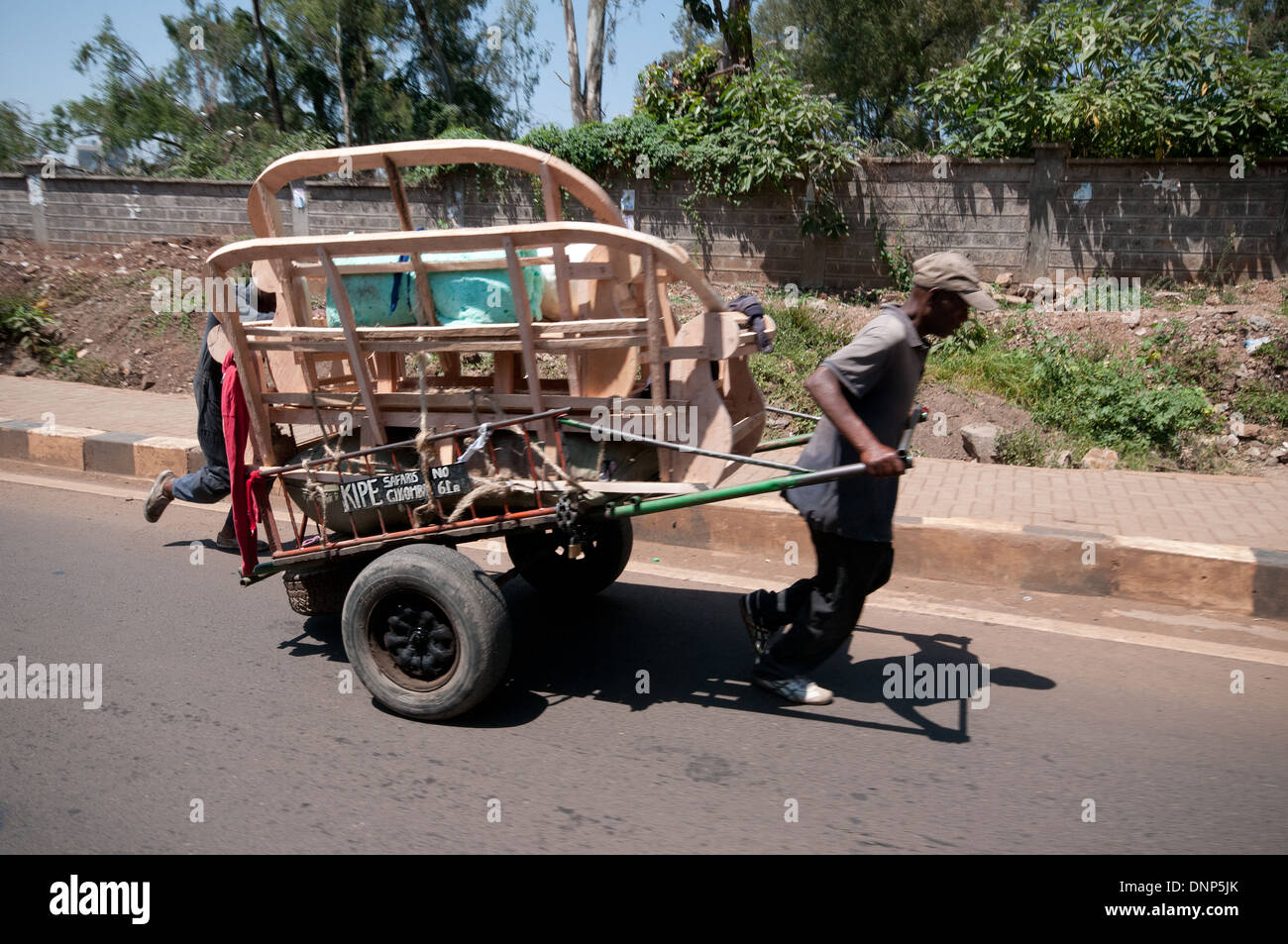 Gli uomini lottano con molto carico carrello portante mobili su strada forestale Nairobi Kenya Nairobi Kenya carrello trasporto del carrello Foto Stock