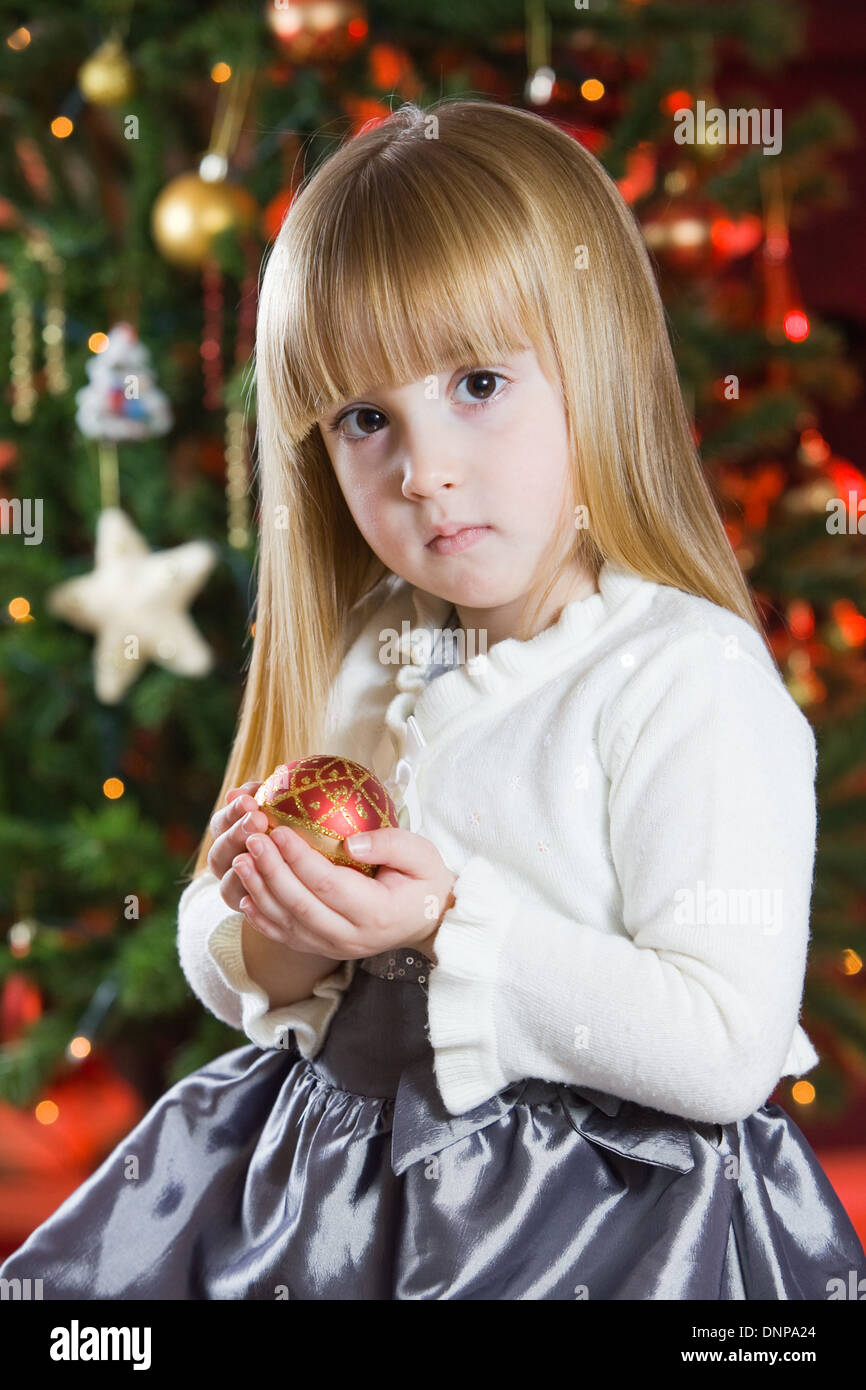 Una bambina di tre anni con un albero di Natale dietro di lei Foto Stock