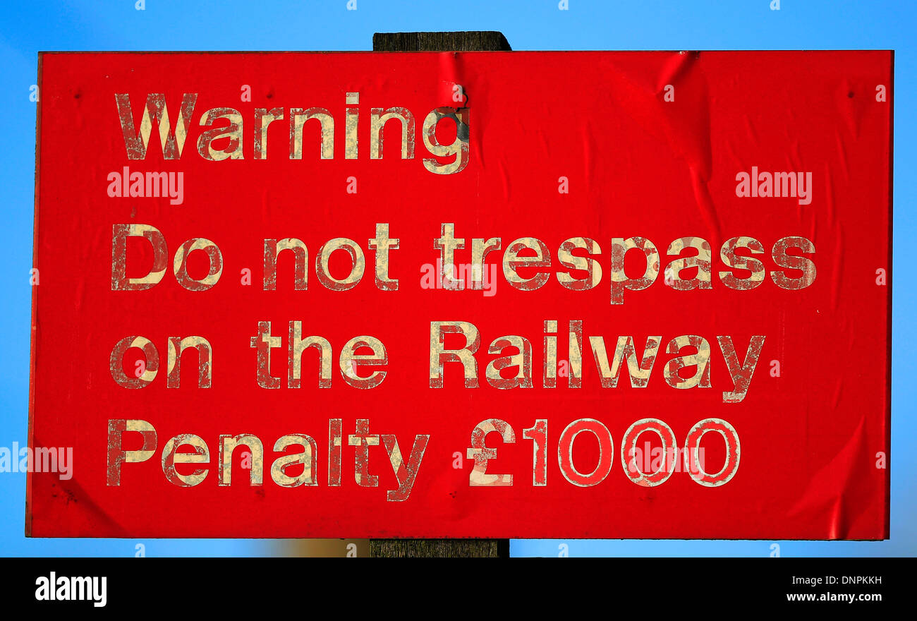 Spia rossa segno: 'non sconfinare sulla ferrovia, pena £1000' attaccato ad un palo e impostare contro un cielo blu Foto Stock