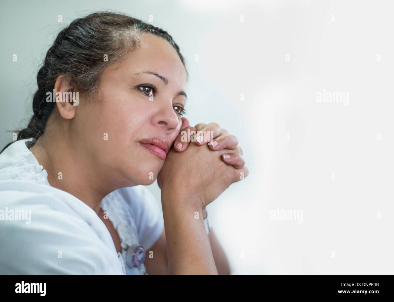 Contemplativa donna ispanica contro uno sfondo luminoso Foto Stock