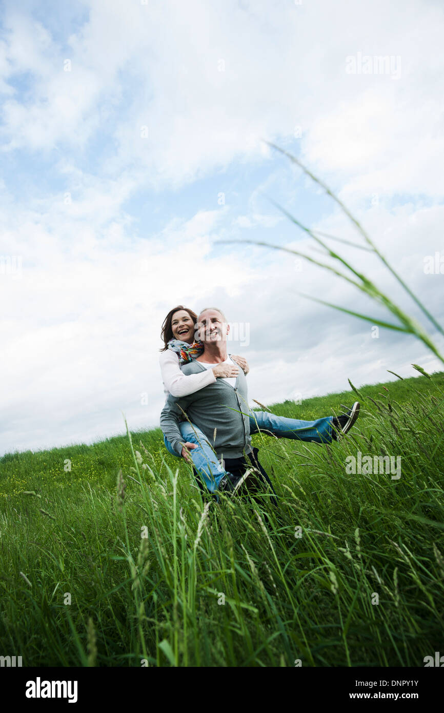 Coppia matura nel campo di erba, uomo dando piggyback ride per donna, Germania Foto Stock