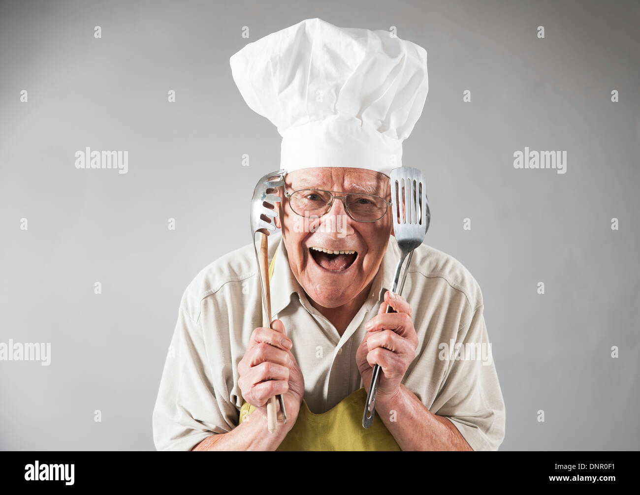 Senior Uomo con utensili da cucina che indossa il grembiule e dallo Chef Hat, Studio Shot Foto Stock