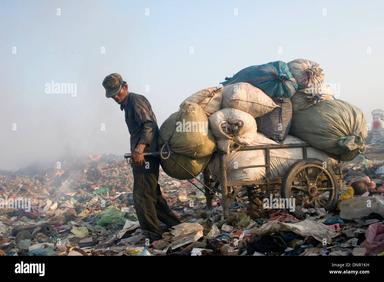 Un lavoratore di sesso maschile cale di materiale riciclabile con un carrello di acciaio presso il pungo Meanchey discarica in Phnom Penh Cambogia. Foto Stock
