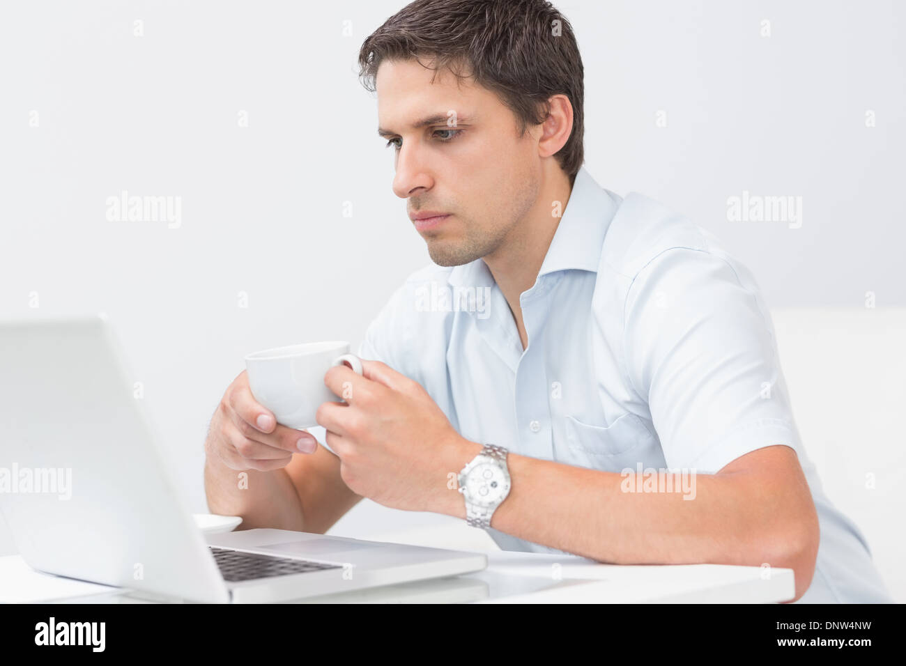 Uomo serio con tazzina utilizzando portatile a casa Foto Stock