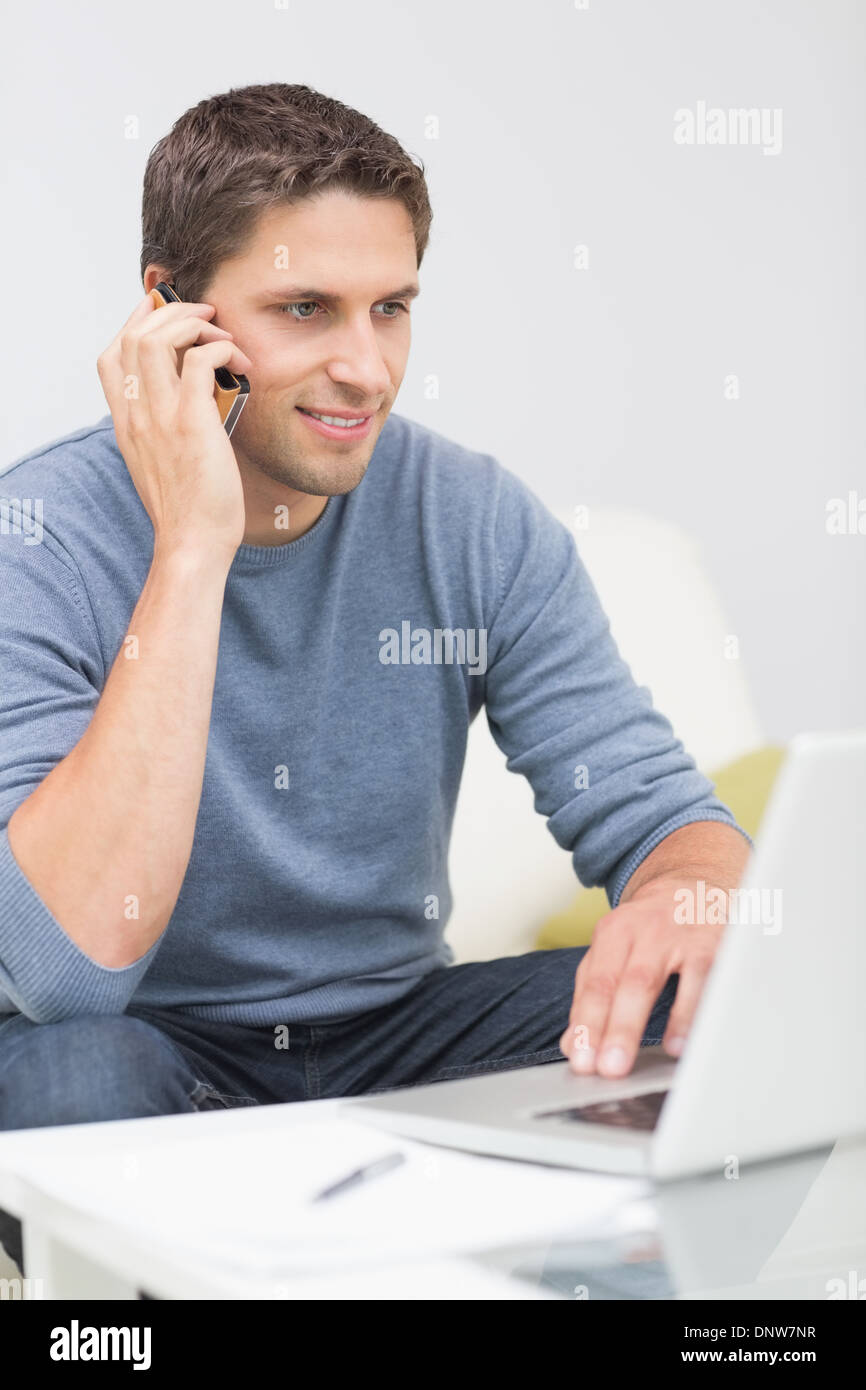 Uomo che utilizza il cellulare e il computer portatile in salotto Foto Stock