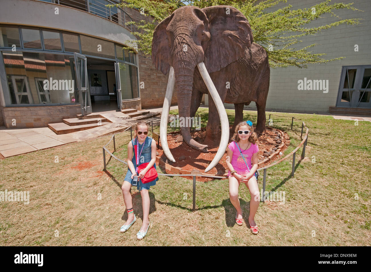 Due white Caucasian ragazze pongono dalla dimensione di vita effige di Ahmed famoso elefante di Marsabit in Nairobi Museo Nazionale del Kenya Foto Stock