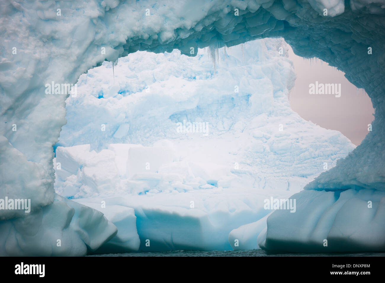 Antartide - un grande buco scavato al di fuori di un iceberg antartico, con una seconda grande iceberg visibile attraverso il foro. Curtis Bay, l'Antartide. Foto Stock