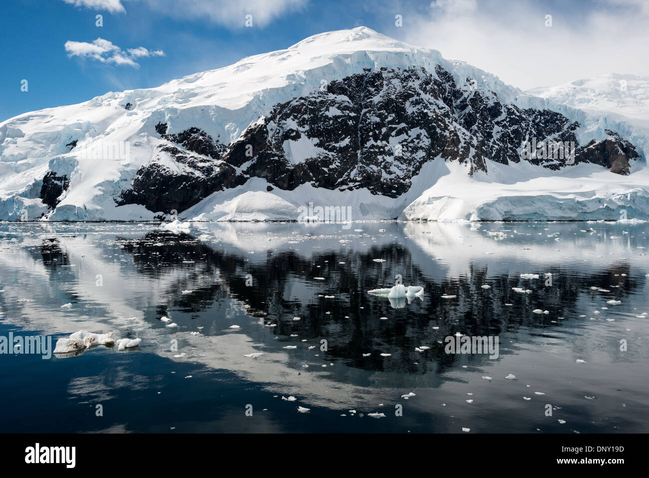 Antartide - il gelido e rocky scenic paesaggio montagne coperte di neve e ghiaccio a Neko Harbour sulla penisola Antartico è riflessa su specchio vetroso-come acque calme. Foto Stock