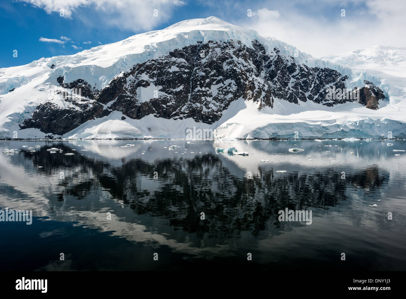 Antartide - il gelido e rocky scenic paesaggio montagne coperte di neve e ghiaccio a Neko Harbour sulla penisola Antartico è riflessa su specchio vetroso-come acque calme. Foto Stock