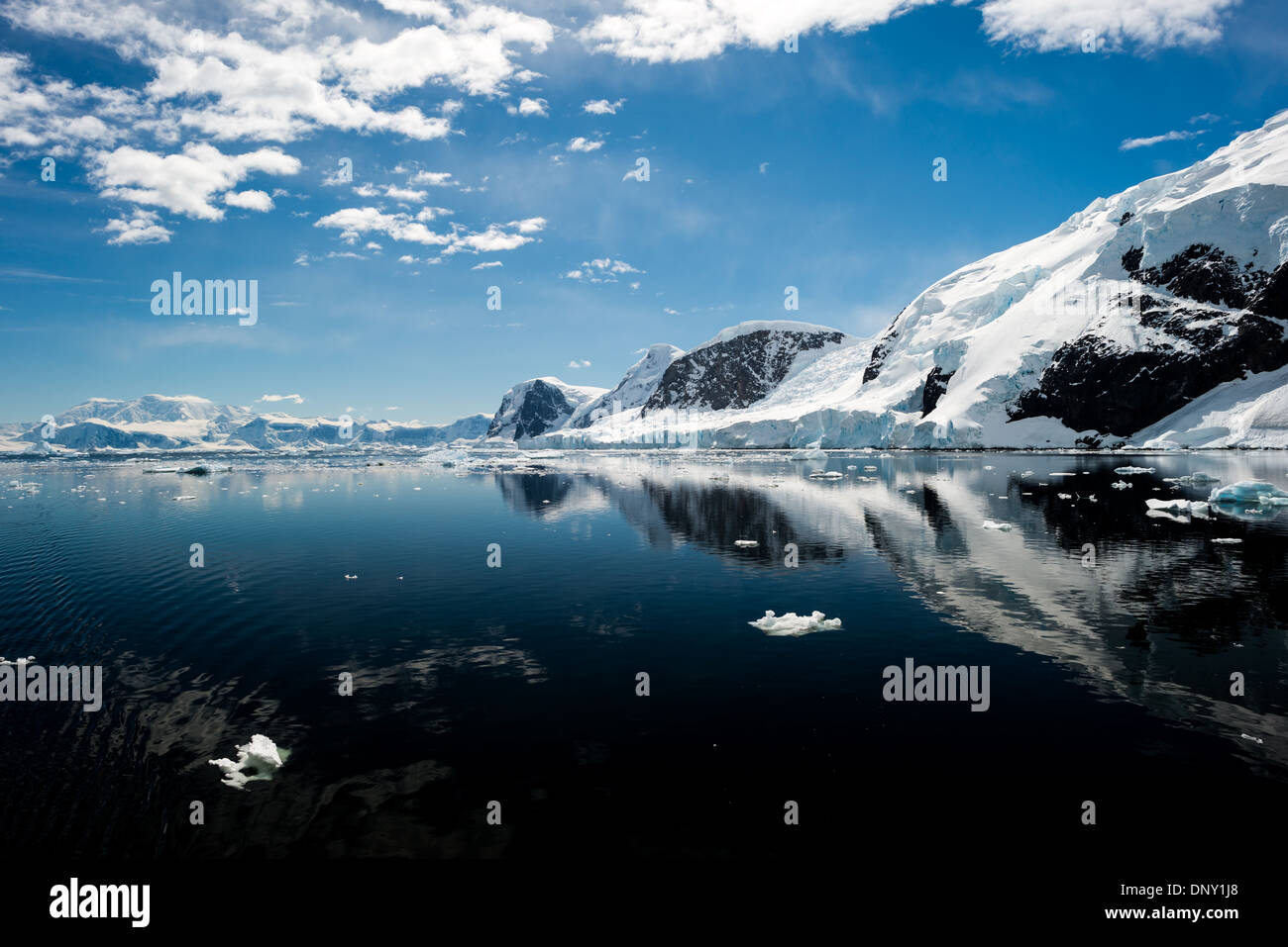 Antartide - il gelido e rocky scenic paesaggio montagne coperte di neve e ghiaccio a Neko Harbour sulla penisola Antartico è riflessa su specchio vetroso-come acque calme. Foto Stock