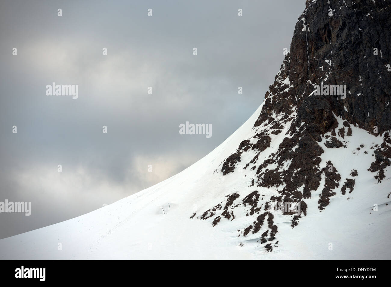 Antartide - una pendenza di curva di ghiaccio e neve porta fino a un vicino alla verticale parete rocciosa faccia su una delle suggestive montagne di rivestimento del litorale della Lemaire Channel in Antartide. Foto Stock