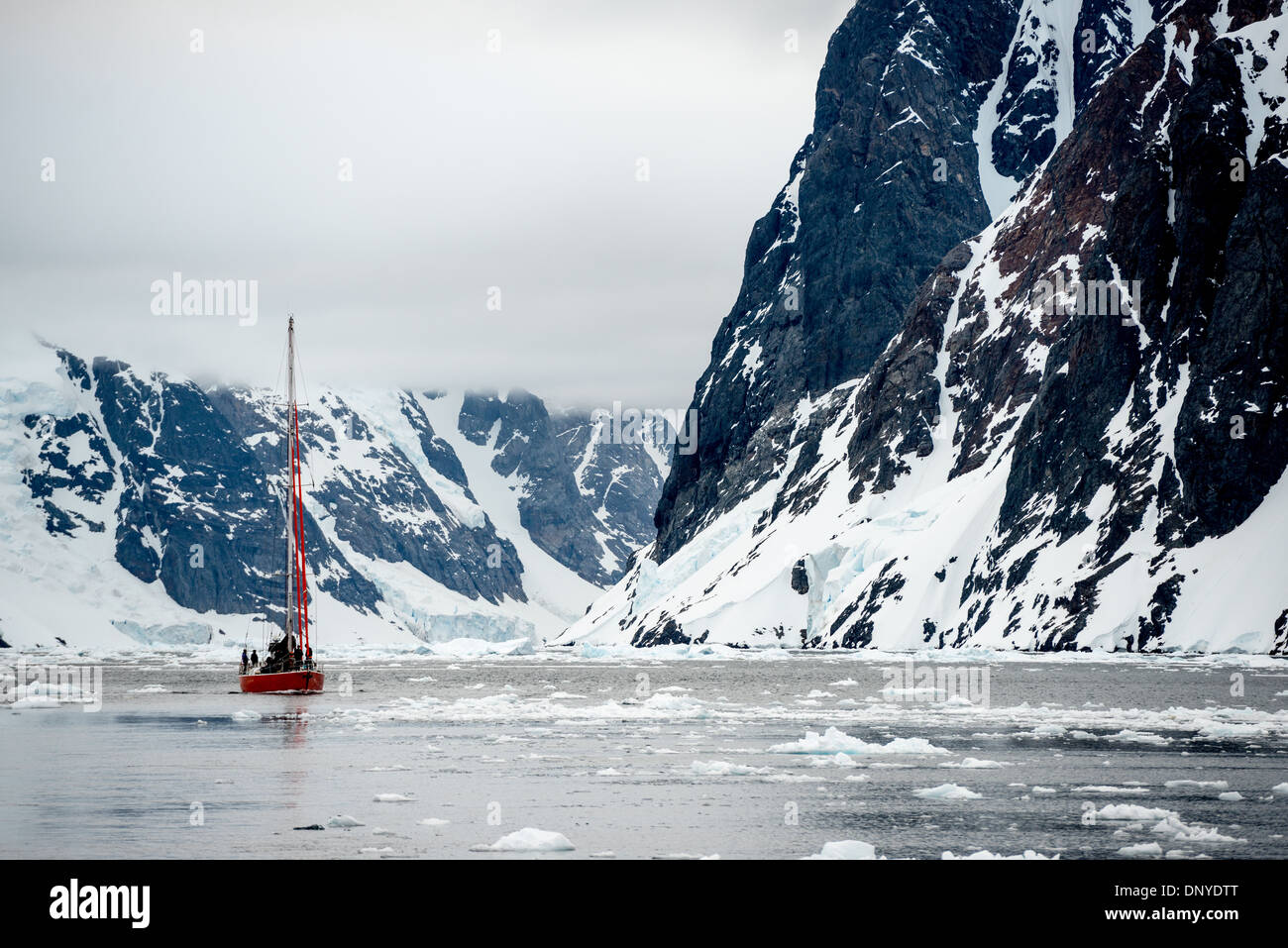 Lemaire Channel Sailboat and Ice Antarctica // [Lemaire Channel Antartide] [Lemaire Channel Antarctic Peninsula] [Kyiv Peninsula] LEMAIRE CHANNEL, Antartide — Una barca a vela naviga con attenzione attraverso il ghiaccio lungo le ripide scogliere rocciose del Lemaire Channel. Questo stretto passaggio lungo la Penisola Antartica, soprannominato "Kodak Gap", presenta sfide uniche per le imbarcazioni a vela mentre manovrano attraverso le diverse condizioni di ghiaccio tra le torreggianti pareti del canale. Foto Stock
