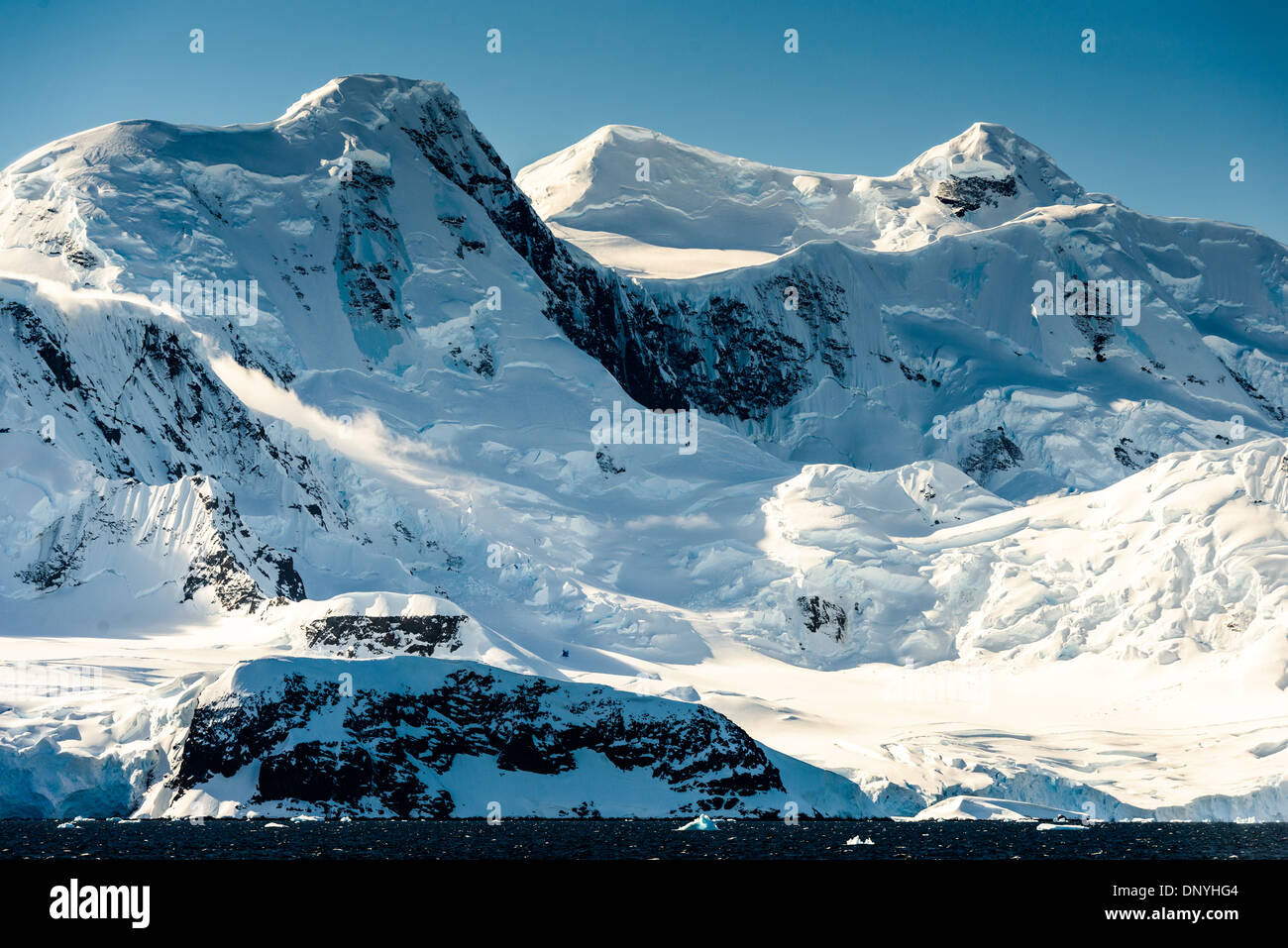 Stretto di Gerlache Montagne innevate Antartide // STRETTO DI GERLACHE, Antartide - neve spettacolare e montagne ricoperte di ghiaccio si innalzano dalla costa dello stretto di Gerlache sulla costa occidentale della Penisola Antartica. Questa regione è conosciuta per i suoi paesaggi mozzafiato ed è un percorso popolare per le crociere in Antartide, che offre l'opportunità di osservare diversi animali selvatici e paesaggi mozzafiato. Lo stretto è situato tra l'arcipelago Palmer e la penisola antartica, fornendo un passaggio naturale per le navi che navigano nelle acque ghiacciate. Foto Stock