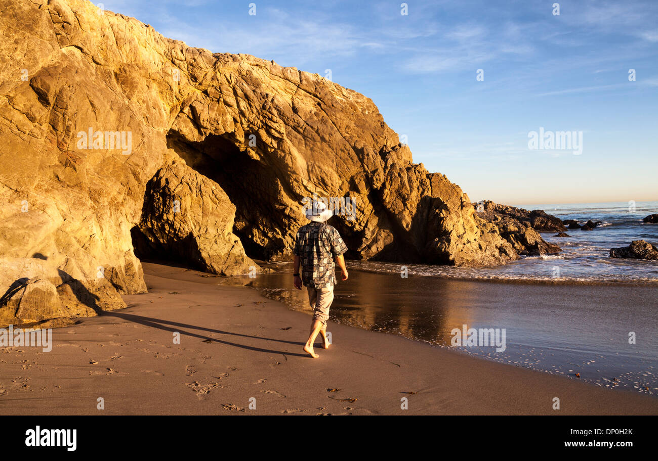 L'uomo cammina verso il mare di grotte e scogliere a dog-friendly area di Leo Carillo State Beach in California del Sud al tramonto Foto Stock