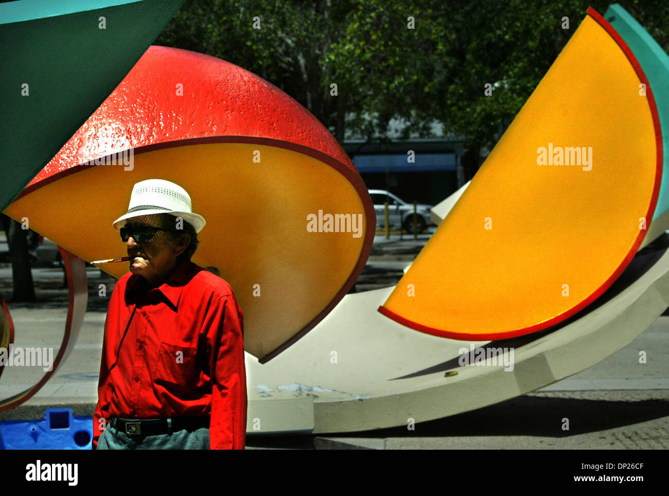 Maggio 18, 2006; Miami, FL, Stati Uniti d'America; sigaretta tenuto elegantemente in un supporto, residente a Miami Divaldo Diaz passeggiate passato due grandi fette di arancio situato al di fuori della Stephen P. Clark Centro di governo su NW prima strada. Le sezioni di colore arancione sono parte di un più grande scultura realizzata nel 1990 dal team artista Claes Oldenburg e Coosje van Bruggen. La scultura/fontana (la fontana non è stato lavoro Foto Stock