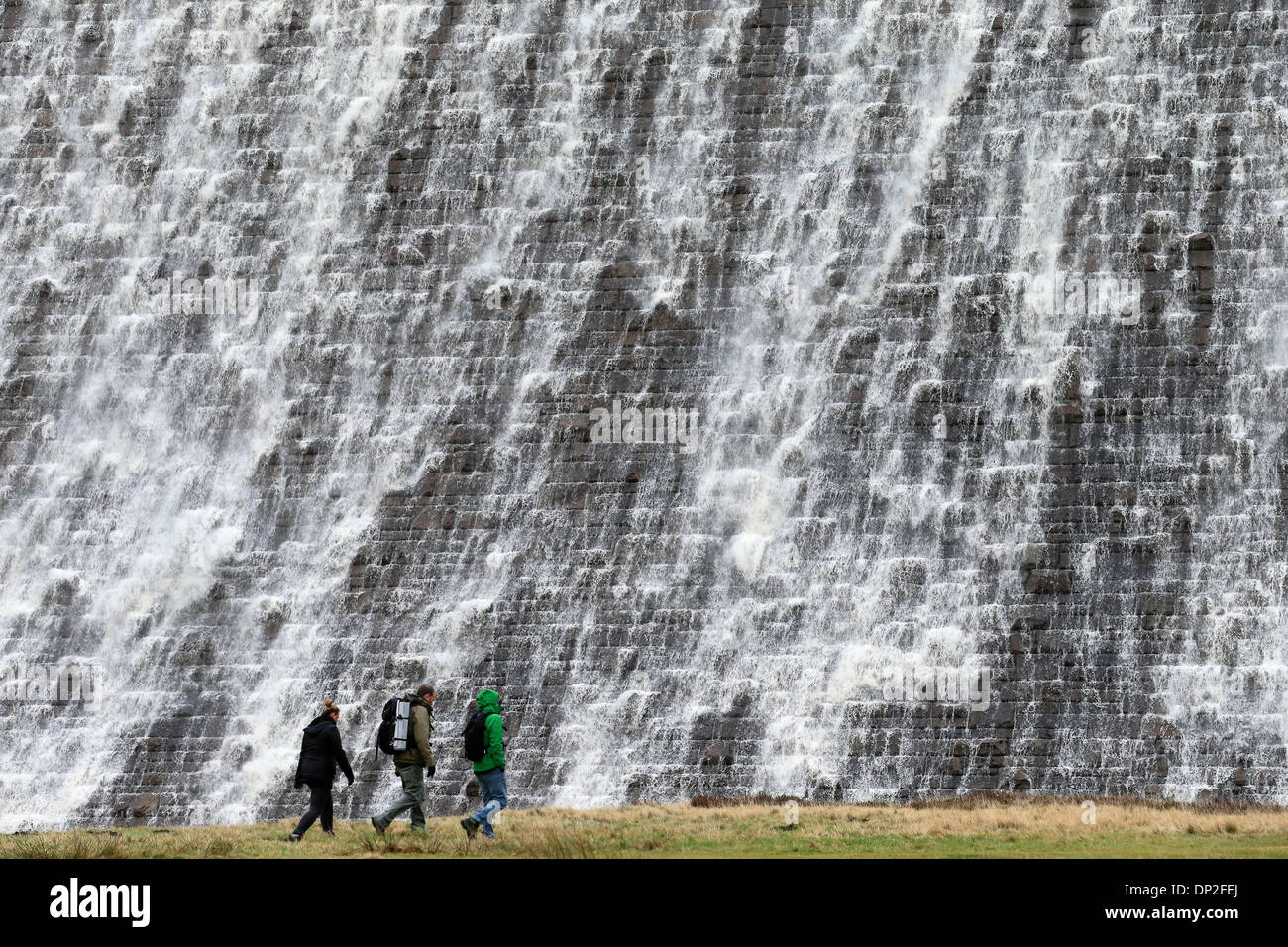 Il Peak District, Derbyshire, Regno Unito. Il 7 gennaio 2014. Dopo giorni di pioggia pesante, escursionisti sono sopraffatte da una parete d'acqua che trabocca dalla Derwent serbatoio sopra la diga Derwent nel Derbyshire Peak District. La diga è uno dei tre nella Derwent Vally che è stato reso famoso dalla Dambusters missioni di addestramento. Credito: Joanne Roberts/Alamy Live News Foto Stock