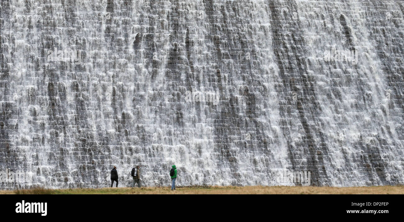 Il Peak District, Derbyshire, Regno Unito. Il 7 gennaio 2014. Dopo giorni di pioggia pesante, escursionisti sono sopraffatte da una parete d'acqua che trabocca dalla Derwent serbatoio sopra la diga Derwent nel Derbyshire Peak District. La diga è uno dei tre nella Derwent Vally che è stato reso famoso dalla Dambusters missioni di addestramento. Credito: Joanne Roberts/Alamy Live News Foto Stock