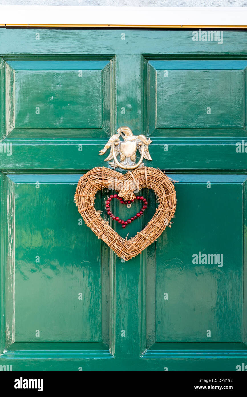 A forma di cuore ad ghirlanda di Natale appeso alla porta verde sotto ornati porta in ottone respingente a forma di L'Aquila Foto Stock
