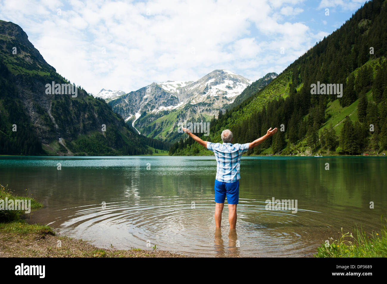 Backview dell uomo maturo con braccia tese verso l'esterno, in piedi nel lago Vilsalpsee, Valle di Tannheim, Austria Foto Stock