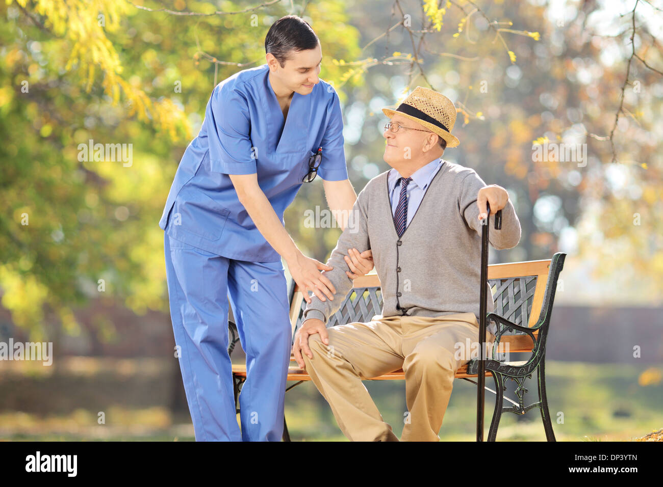 Professionista del healthcare parlando con i senior uomo seduto su un banco di lavoro al di fuori Foto Stock