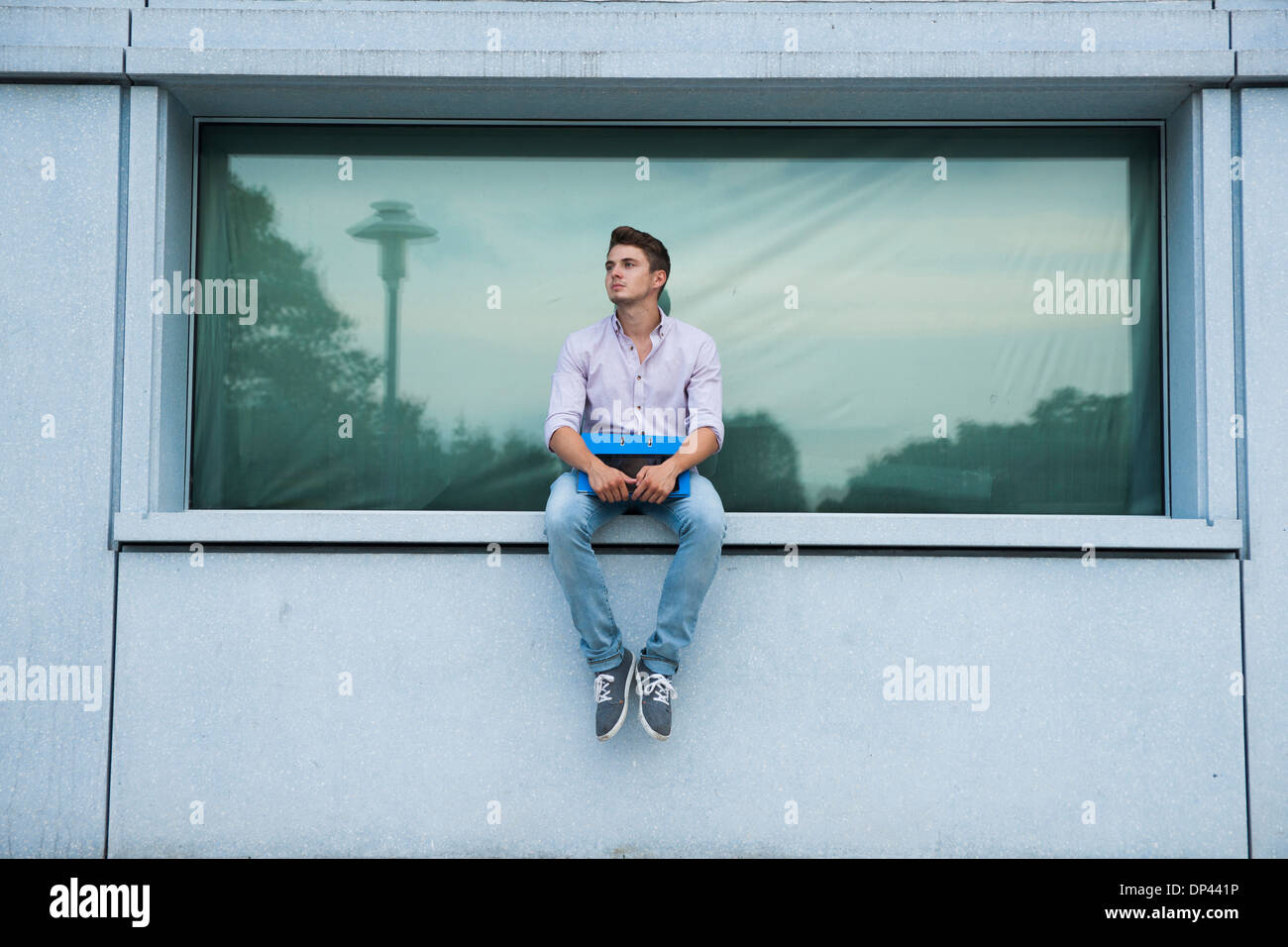 Giovane uomo seduto sulla mensola all'aperto, Germania Foto Stock