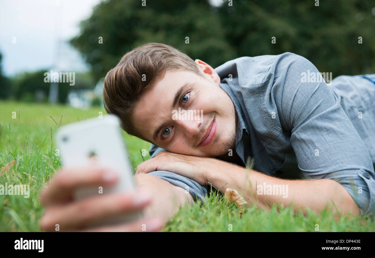 Close-up di giovane uomo disteso su erba, guardando il telefono cellulare, Germania Foto Stock