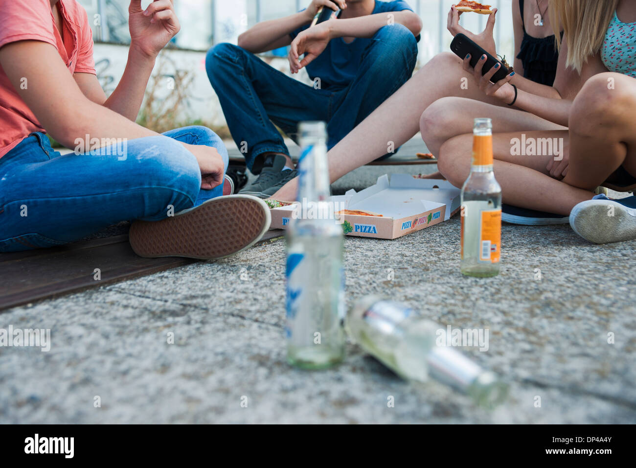 La superficie di visualizzazione a livello di gruppo di adolescenti seduti su un terreno aperto, di mangiare la pizza e appendere fuori, Germania Foto Stock