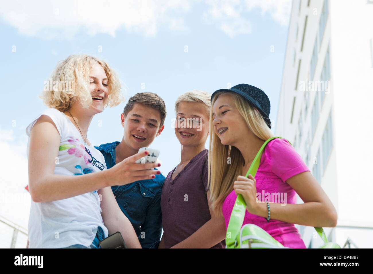 Gruppo di adolescenti in piedi all'esterno guardando al telefono cellulare e parlare, Germania Foto Stock