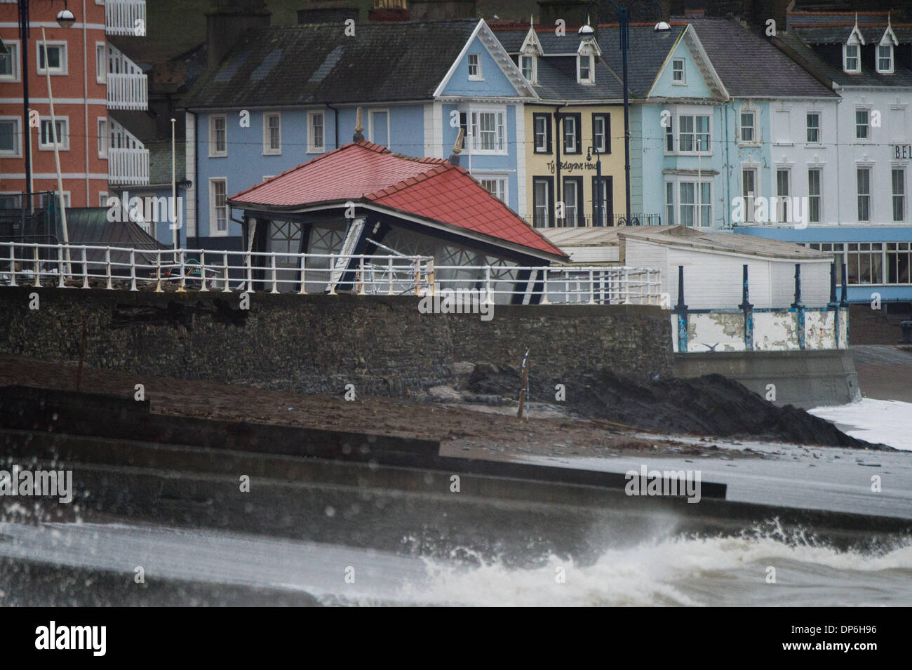 Aberystwyth, Wales, Regno Unito. 8 gennaio 2014. L'iconico pubblica gli elenchi di ricovero precariamente come l'operazione di pulizia continua a Aberystwyth dopo giorni di maltempo gravemente danneggiato la promenade. Le autorità locali ha chiuso fuori della zona per consentire il lavoro di procedere con sicurezza, permettendo l'impiego di macchinari pesanti per cancellare le centinaia di tonnellate di e e di macerie e di estrarre la pavimentazione in lastre e ciottoli che si erano formate sulla superficie del lungomare Photo credit: keith morris/Alamy Live News Foto Stock