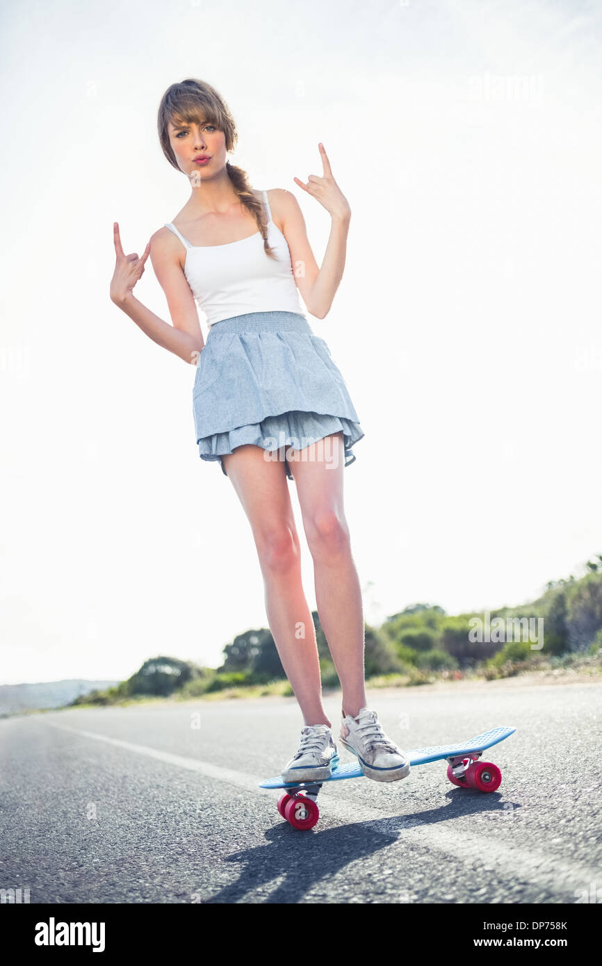 Giovane donna fare rock and roll gesto mentre il bilanciamento sul suo skateboard Foto Stock