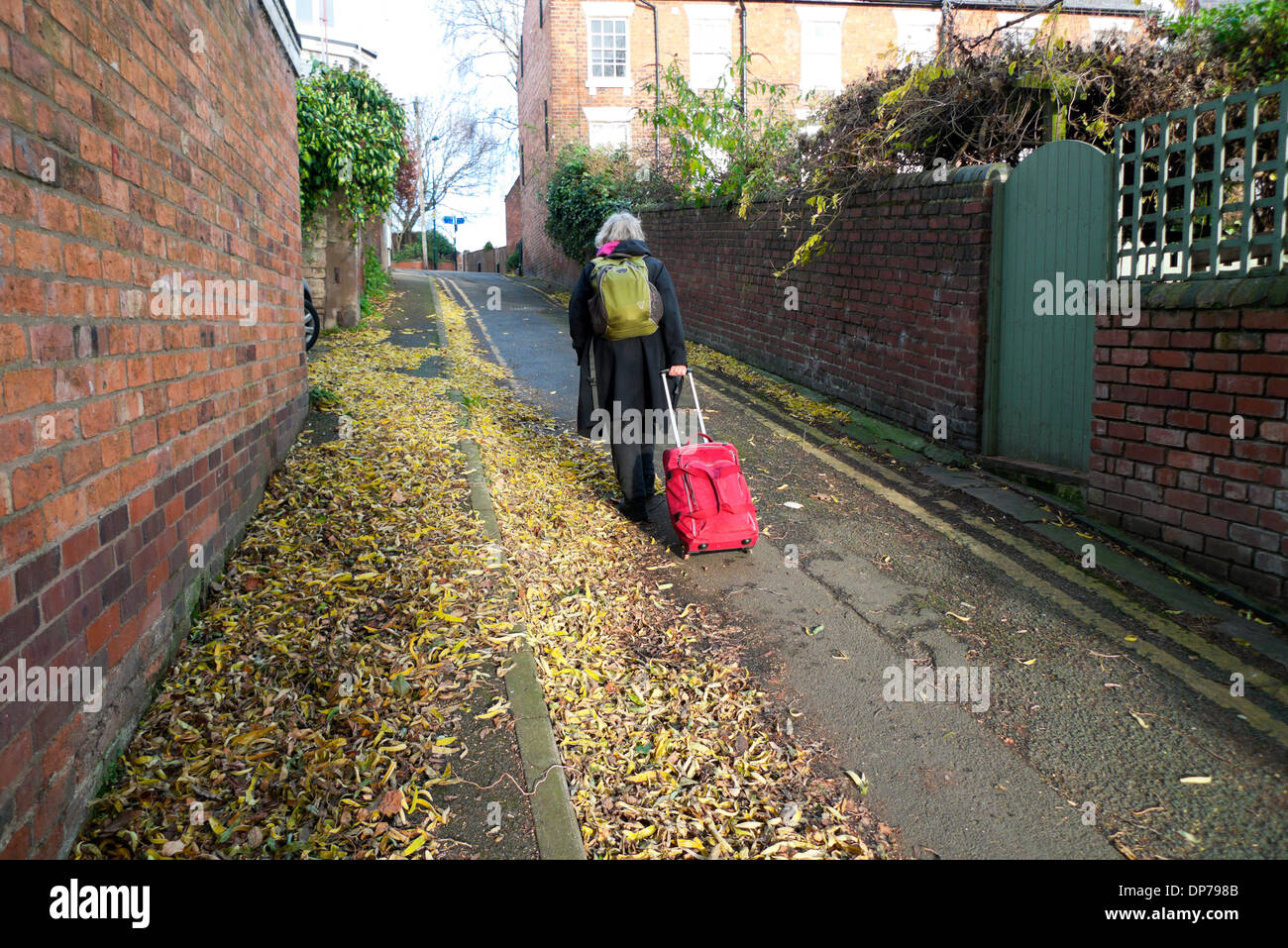 Una donna anziana con un zaino verde e rosso sacchetto bagagli camminare su per una collina a Shrewsbury Shropshire England Regno Unito KATHY DEWITT Foto Stock
