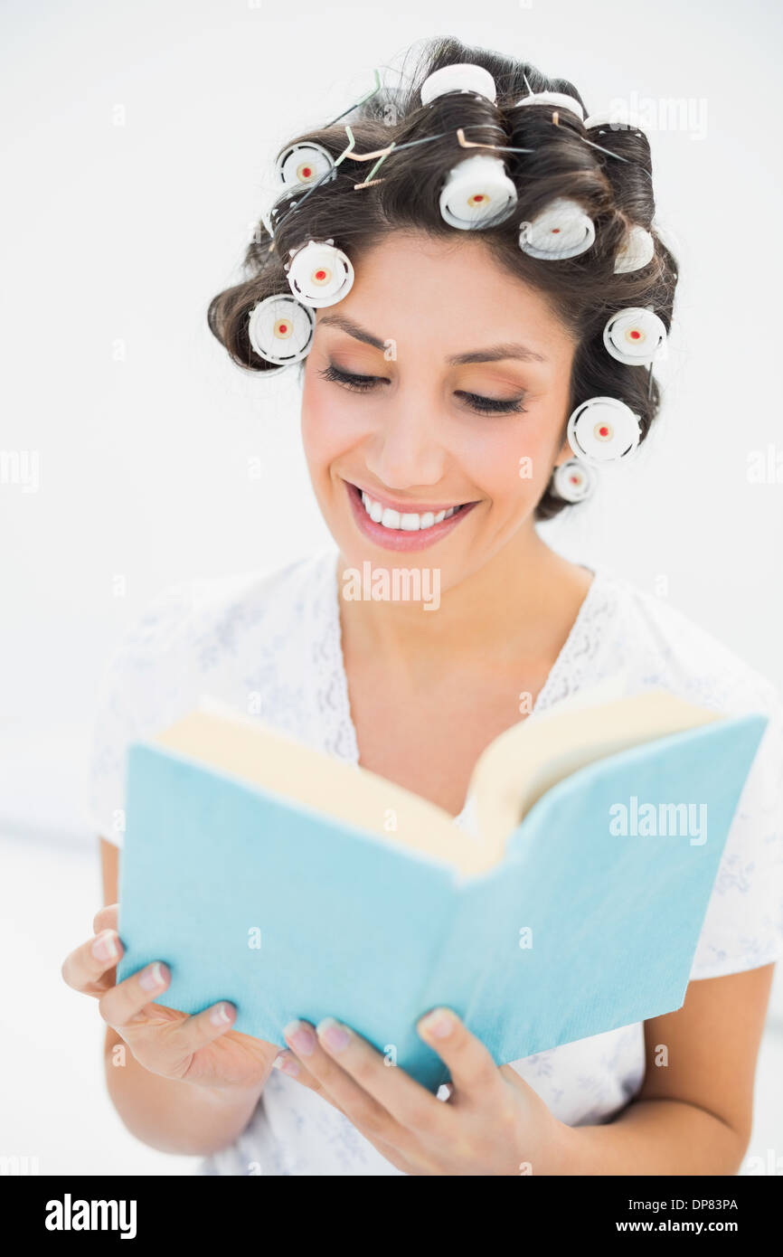 Allegro brunette nei capelli rulli a leggere un libro sul letto Foto Stock