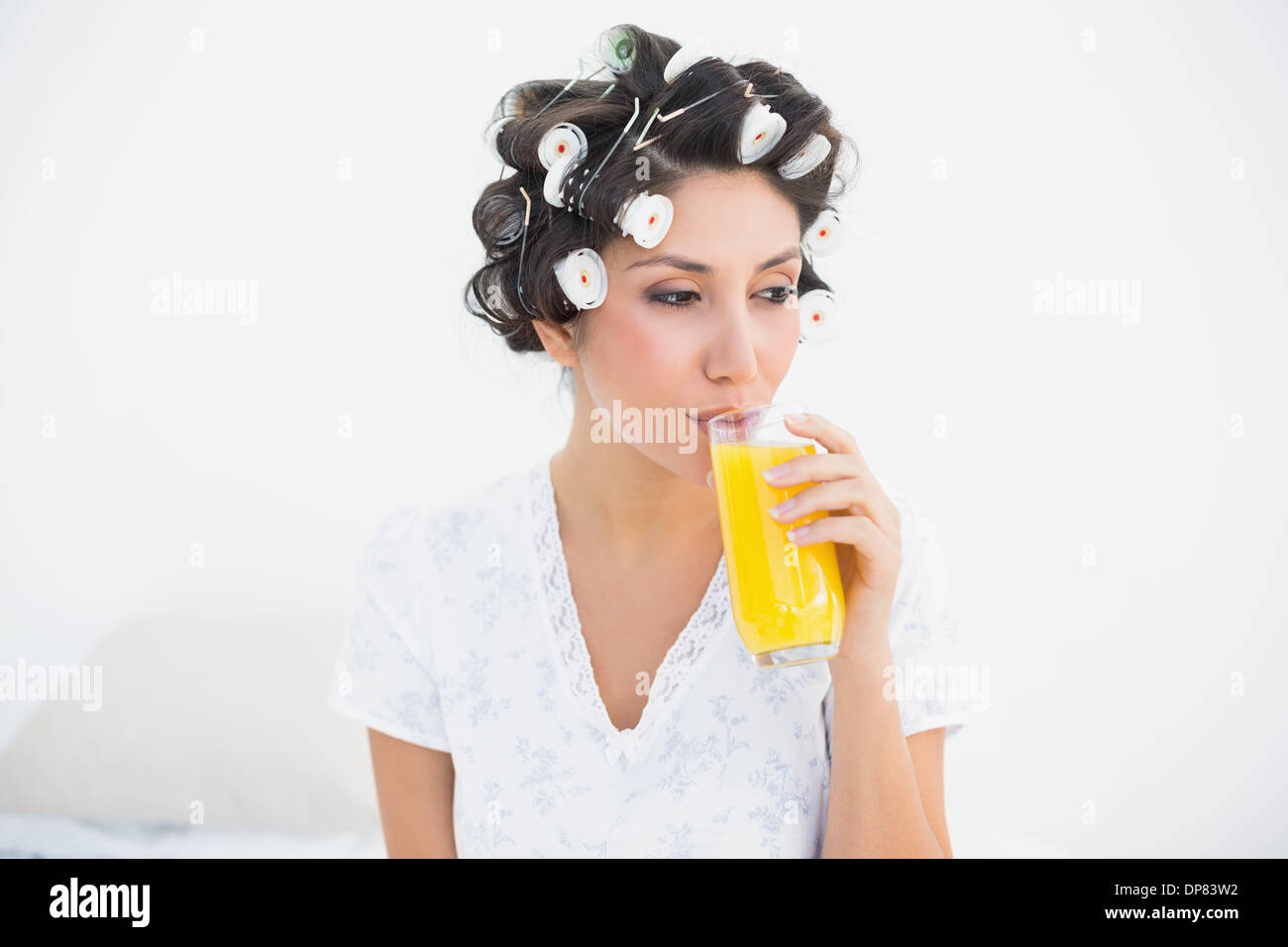 Bella bruna nei capelli rulli di bere un bicchiere di succo di arancia Foto Stock