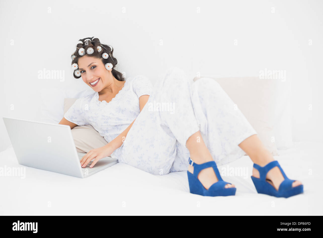 Bruna nei capelli rulli e scarpe a cuneo con il suo computer portatile sul letto Foto Stock
