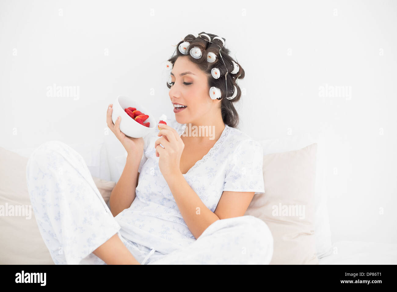 Sorridente brunette nei capelli rulli aventi una tazza di fragole Foto Stock