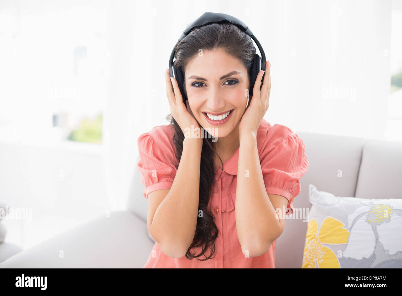 Happy brunette seduta sul suo divano ascolto di musica Foto Stock