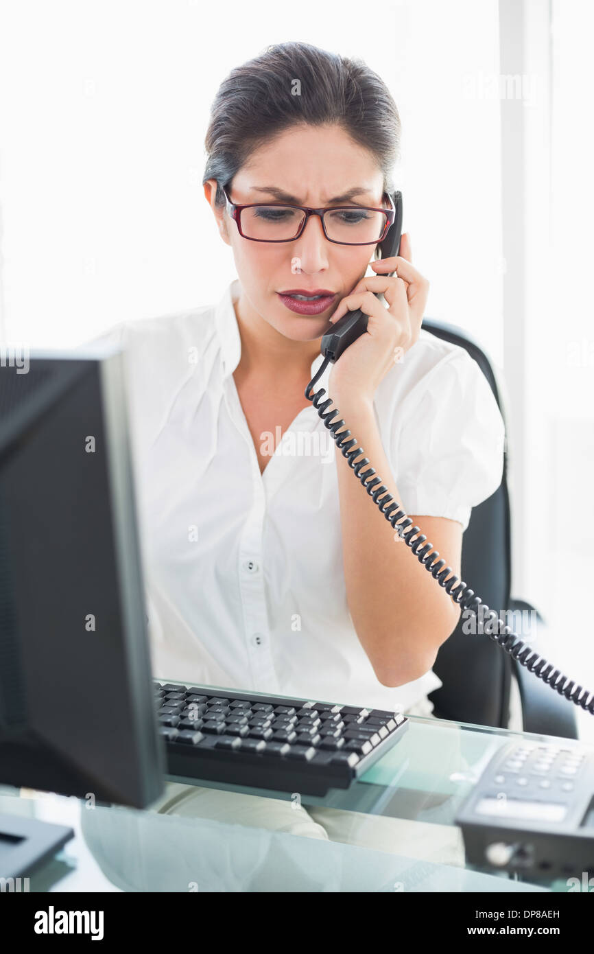 Accigliata imprenditrice seduto alla sua scrivania parlando al telefono Foto Stock
