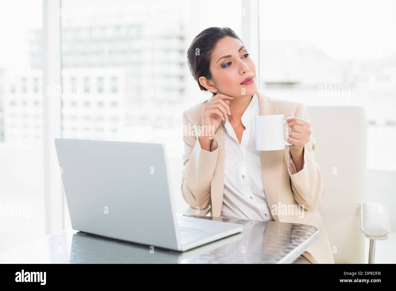 Riflessivo imprenditrice tenendo la tazza mentre si lavora sul computer portatile Foto Stock